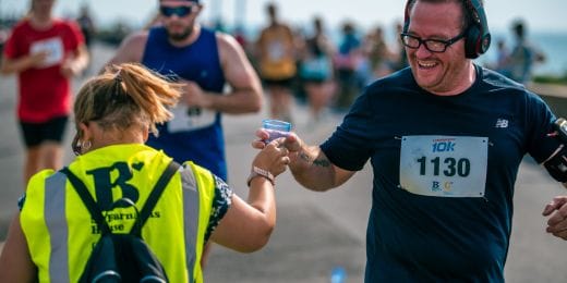 Smiling runner receives water from a volunteer during a charity event, representing volunteering for Southern Hospice Group.